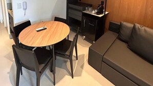 A modern living room with a round wooden table, black chairs, a grey sofa, and a built-in kitchen area with a wooden finish. - Porto 2 Life Resort (Ipojuca)