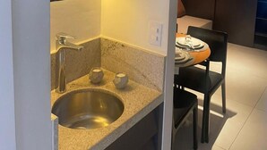 A modern kitchen with a built-in sink, a microwave, and a dining area with a table and chairs. - Porto 2 Life Resort (Ipojuca)