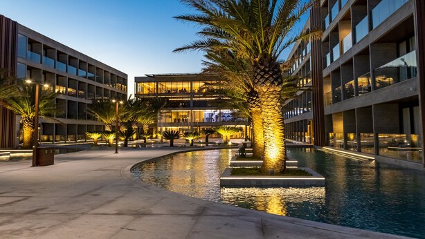 A modern building with a pool, palm trees, and a well-lit walkway. - Porto 2 Life Resort (Ipojuca)