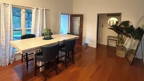 Un comedor con una mesa de madera, sillas, una araña y ventanas amplias.