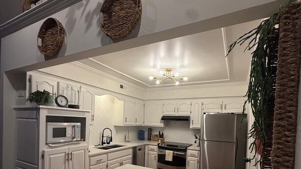 Una cocina moderna con armarios blancos, una isla central y un refrigerador de acero inoxidable.