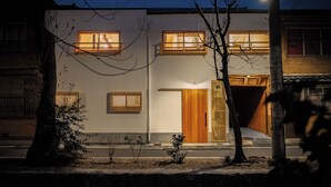 Un edificio moderno con due finestre visibili, una porta in legno e un piccolo albero sullo sfondo.