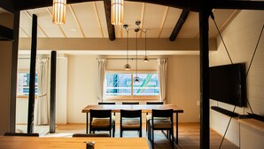 Un'area pranzo con tavolo in legno, sedie, lampade a sospensione, una finestra con tende e una TV a schermo piatto montata a parete.
