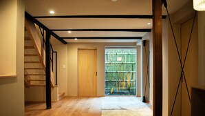 Un corridoio con pavimento in legno, una scala, una porta e una finestra con vista su piante di bambù.