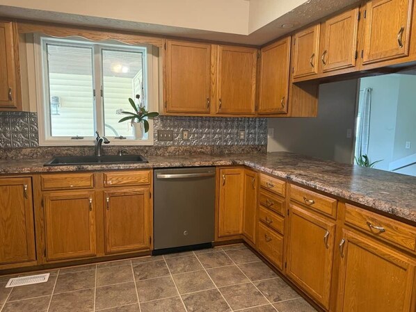 A kitchen with wooden cabinets, a dishwasher, granite countertops, and a window with blinds. - Sleeps 16+ • 5BR • Game Rooms • Near IU/Indy/Lake (Perry Township)