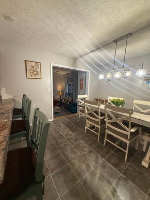 Un comedor con suelo de baldosas, sillas de madera, una mesa y una lámpara colgante.