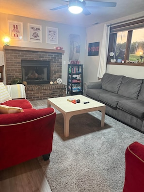 Una sala de estar con chimenea, una estantería, un sofá gris y un sillón rojo.