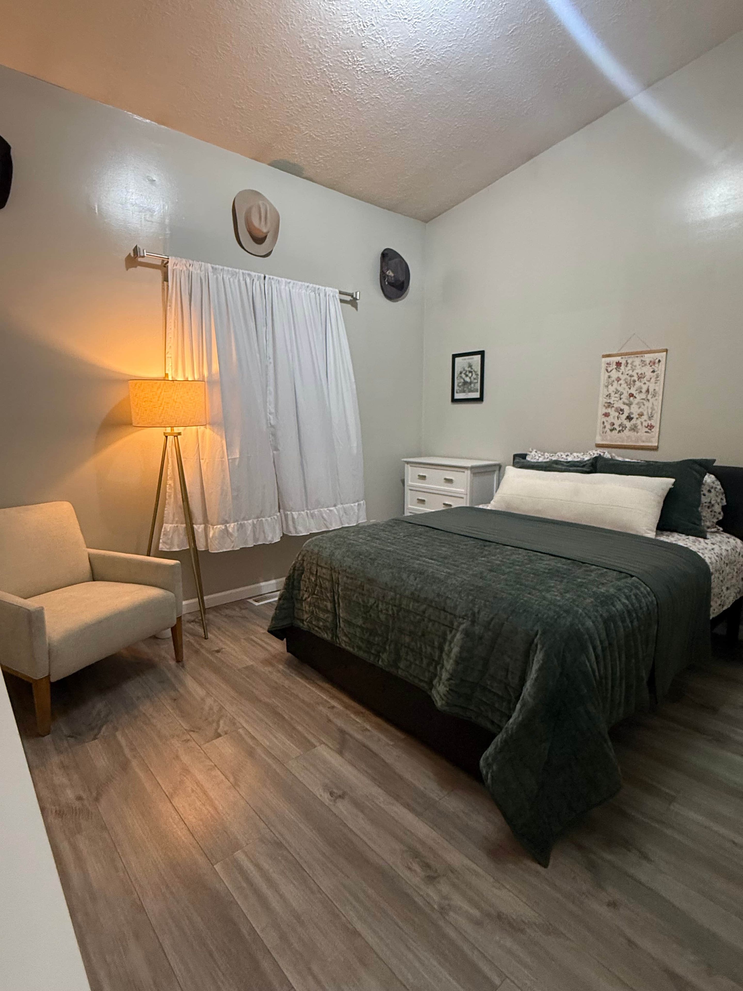 A bedroom with a bed, a chair, a nightstand, a lamp, and a wall-mounted hat.