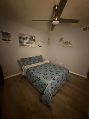 A bedroom with a bed, a ceiling fan, and wall decorations including a painting and a star.