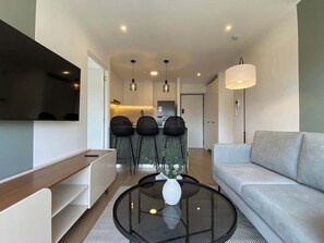 A modern living room with a sofa, a coffee table, and a TV mounted on the wall. - w* | Deluxe 2BR w/ Balcony & View in Miraflores (Miraflores)