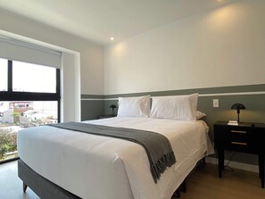 A modern bedroom with a large bed, two bedside tables, a window with a view, and a green accent wall. - w* | Deluxe 2BR w/ Balcony & View in Miraflores (Miraflores)