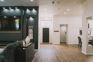A modern living room with a dark accent wall, wooden flooring, a black entertainment unit, and a dining area with a table and chairs. - Modern Pool Retreat: Mid & Long-Term Stays Dallas (Dallas)