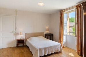A bedroom with a bed, bedside lamps, a window with curtains, and a door.