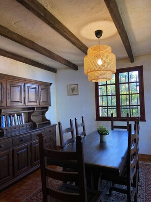 Un espace repas comprenant une table en bois, des chaises, un luminaire suspendu et une fenêtre donnant sur un paysage verdoyant.