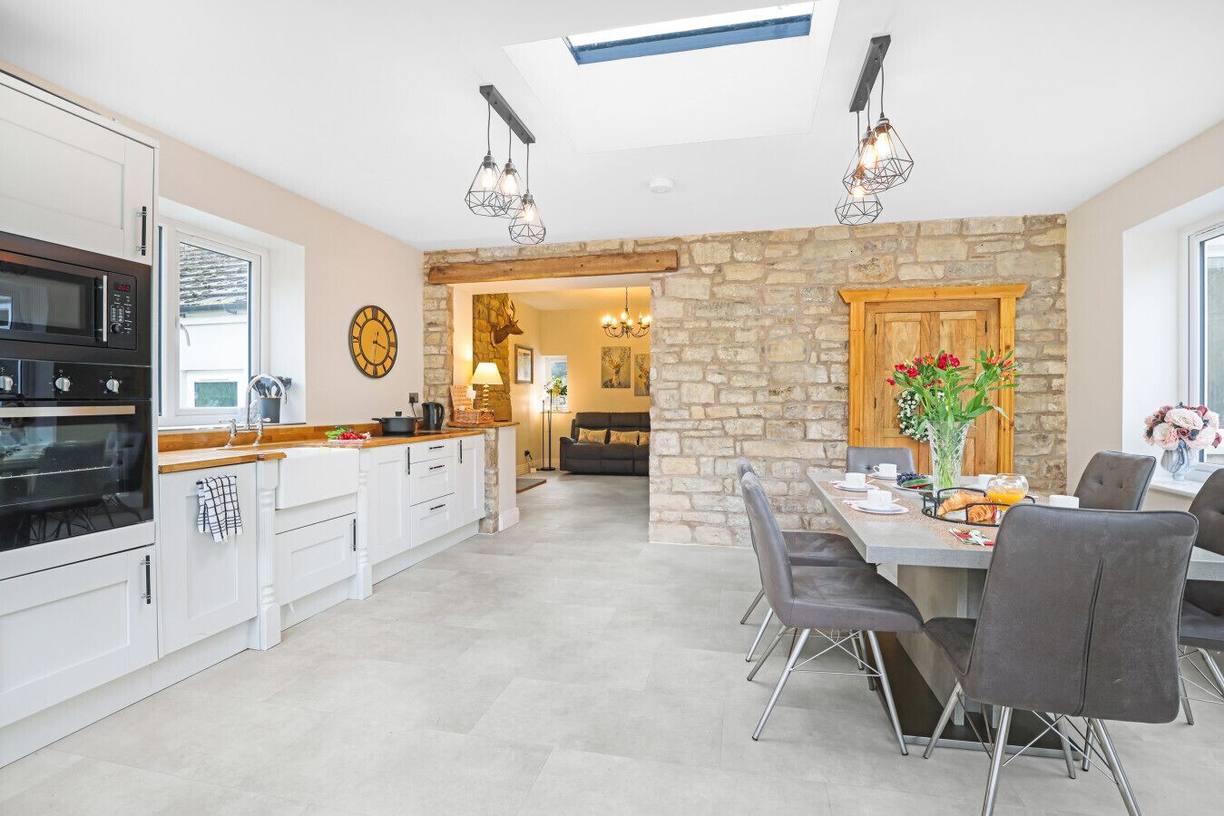 A bright, modern kitchen and dining area with white cabinetry, a stone accent wall, and a cozy view into the living room.
