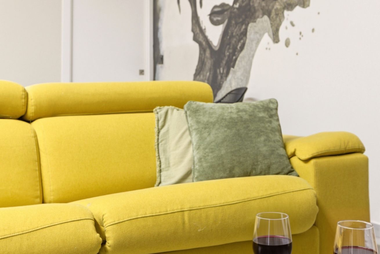 A yellow sofa with a green pillow in a room with a white wall and a black and white artwork.