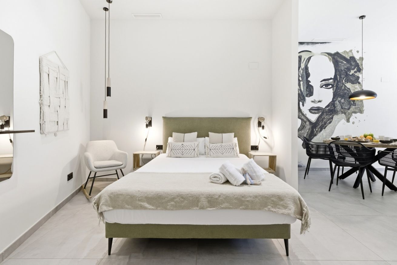 Une chambre moderne avec un grand lit, des lampes de chevet, un fauteuil et un coin repas agrémenté d’une fresque murale.