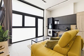 A modern living space with a sofa, a washing machine, and a kitchen area. - Travel Habitat Jardines de Ayora 1 WIFI+AACC (Valencia)