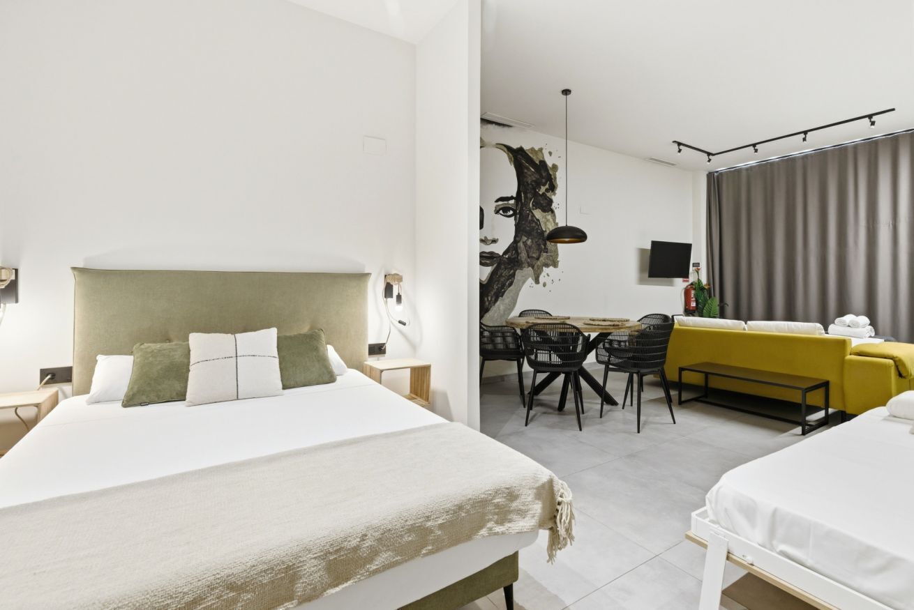 Habitació d'hotel moderna amb un llit gran, una zona de menjador amb taula i cadires, i un sofà.