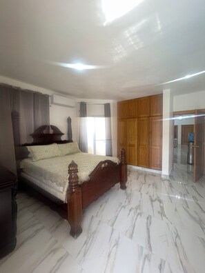 Ein Schlafzimmer mit einem Holzbett, einem Kleiderschrank und einem durch eine offene Tür einsehbaren Badezimmer.