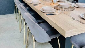 Un comedor moderno con una larga mesa de madera dispuesta para seis personas, sillas grises tapizadas e iluminación colgante.