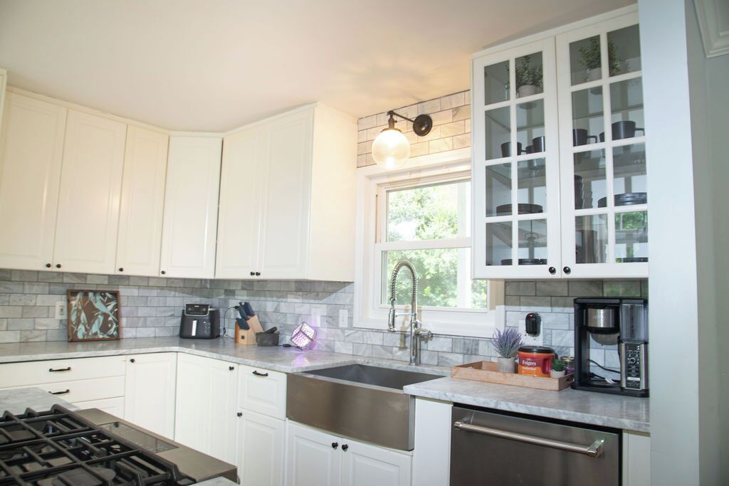 A kitchen with white cabinets, a stainless steel sink, a gas stove, and a coffee maker.