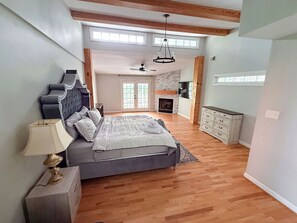 A bedroom with a bed, a nightstand, a lamp, a fireplace, a ceiling fan, and a view of the kitchen. - Five Bedroom Brookview Estate (Atlanta)