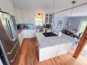 A modern kitchen with white cabinetry, a stainless steel refrigerator, a marble countertop island, and pendant lighting. - Five Bedroom Brookview Estate (Atlanta)
