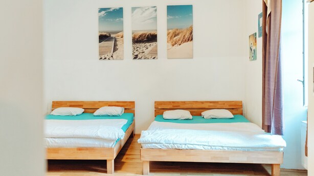 Une pièce avec deux lits en bois, un plancher en bois et un mur orné de trois tableaux encadrés.