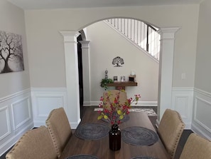 A dining room with a wooden table, beige upholstered chairs, a vase with flowers, and a staircase in the background. - Spacious 5 bedroom (Columbus)