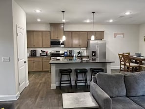 A modern kitchen with a central island, bar stools, a dining area with wooden chairs, and a grey sofa. - Spacious 5 bedroom (Columbus)