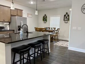 A modern kitchen with a central island, bar stools, wooden chairs, and a dining table. - Spacious 5 bedroom (Columbus)