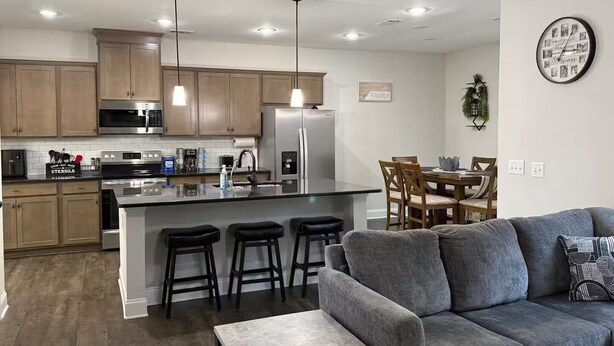Een moderne keuken met roestvrijstalen apparatuur, een centraal kookeiland met barkrukken, en een eethoek met een houten tafel en stoelen.