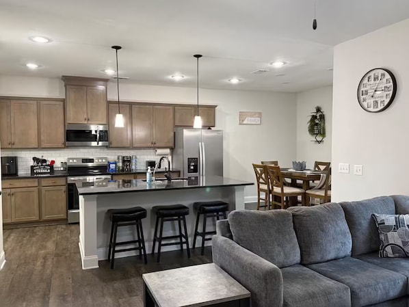 A modern kitchen with stainless steel appliances, a central island with bar stools, and a dining area with a wooden table and chairs. - Spacious 5 bedroom (Columbus)