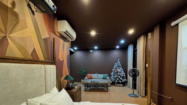 Una habitación de hotel con una cama, una mesita de noche con lámpara, un sofá, un árbol de Navidad y un equipo de aire acondicionado.