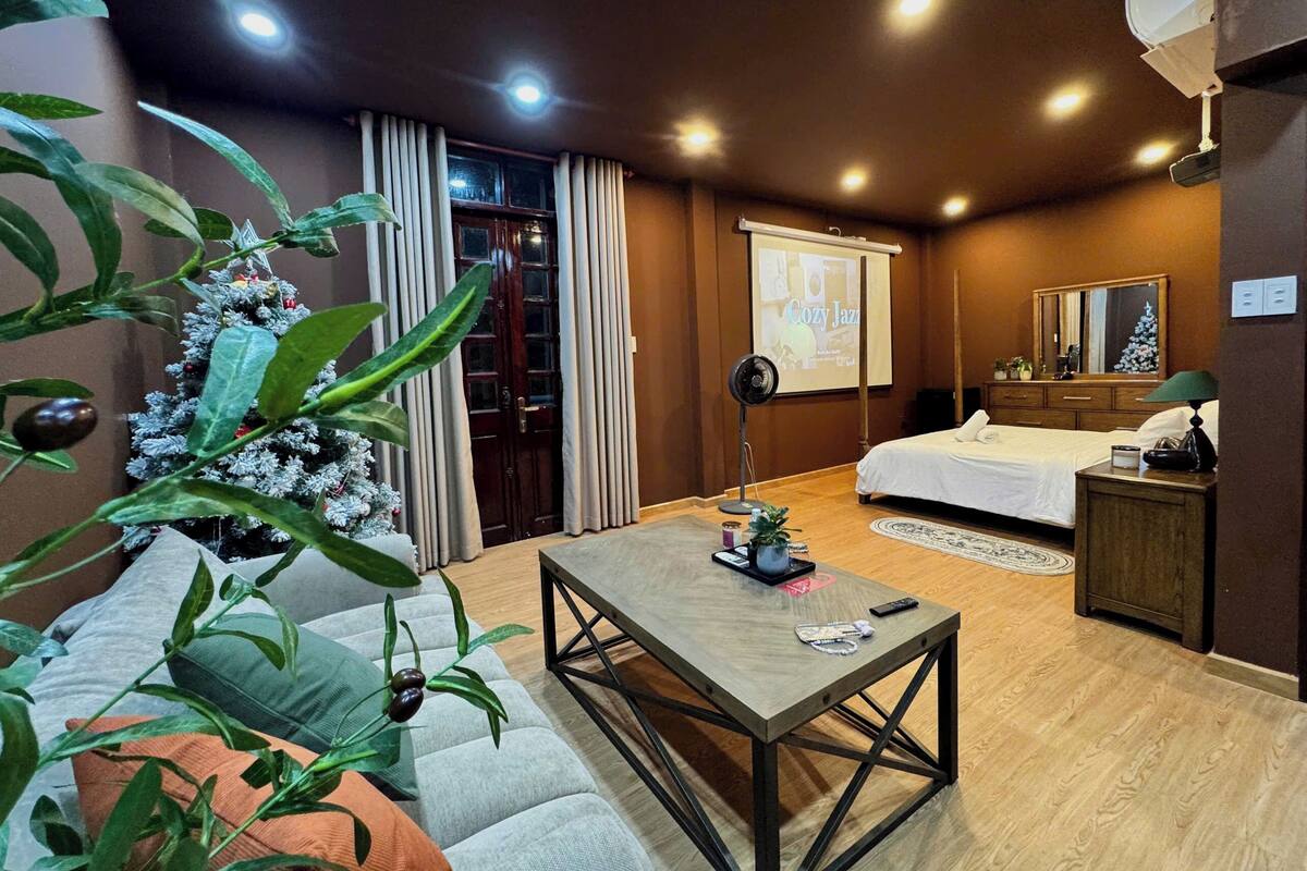 A hotel room with a bed, a desk, a coffee table, and a large plant.