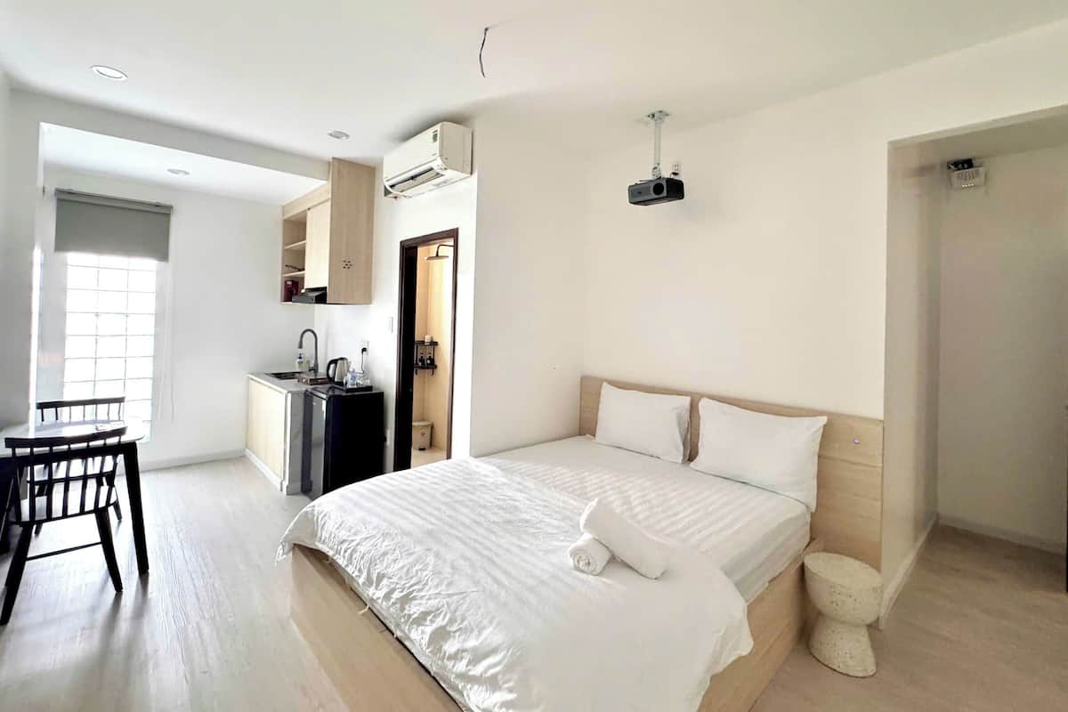 A modern hotel room with a large bed, a small kitchenette, a dining area, and a bathroom.