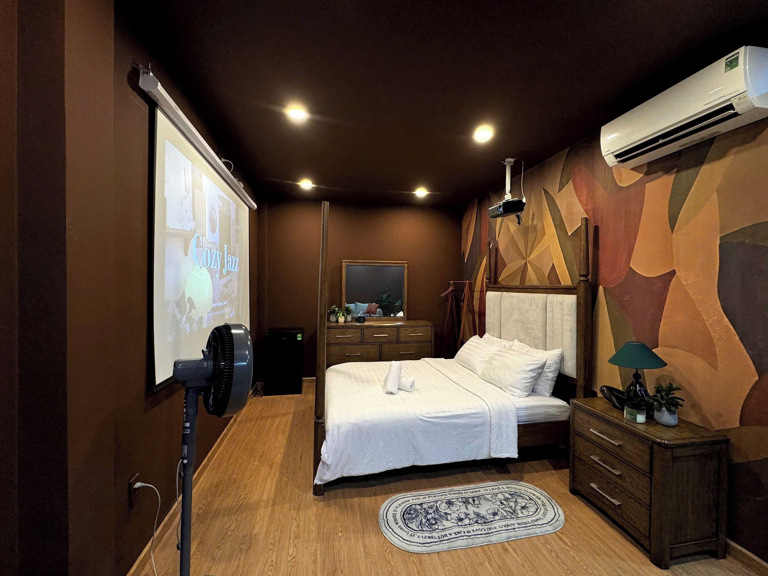 Un dormitorio con cama, cómoda, espejo, unidad de aire acondicionado y pantalla de proyector.