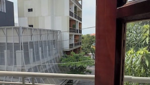 Un balcón con barandilla de metal, vista a un edificio de varios pisos y cielo despejado.