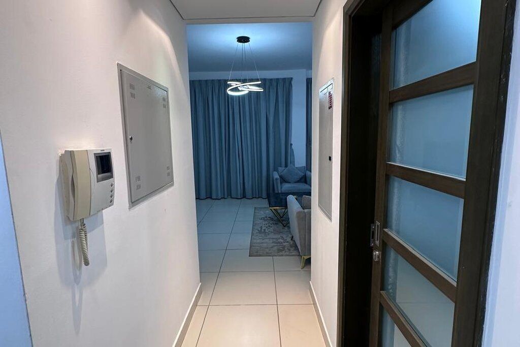 Ein Flur, der zu einem Zimmer mit einem Bett, einem Telefon und einem mit Vorhängen drapierten Fenster führt.