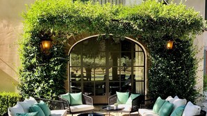 An outdoor seating area with a gravel floor, two sofas with cushions, a small round table, and a decorative archway covered in greenery. - Mas en Provence with swimming pool - comfort and relaxation (Eyragues)