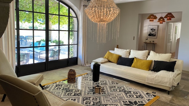 A modern living room with a large arched window, a white sofa with patterned cushions, a hanging chandelier, and a patterned rug. - Mas en Provence with swimming pool - comfort and relaxation (Eyragues)