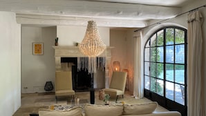 A living room with a fireplace, two chairs, a sofa, and a large window with curtains. - Mas en Provence with swimming pool - comfort and relaxation (Eyragues)