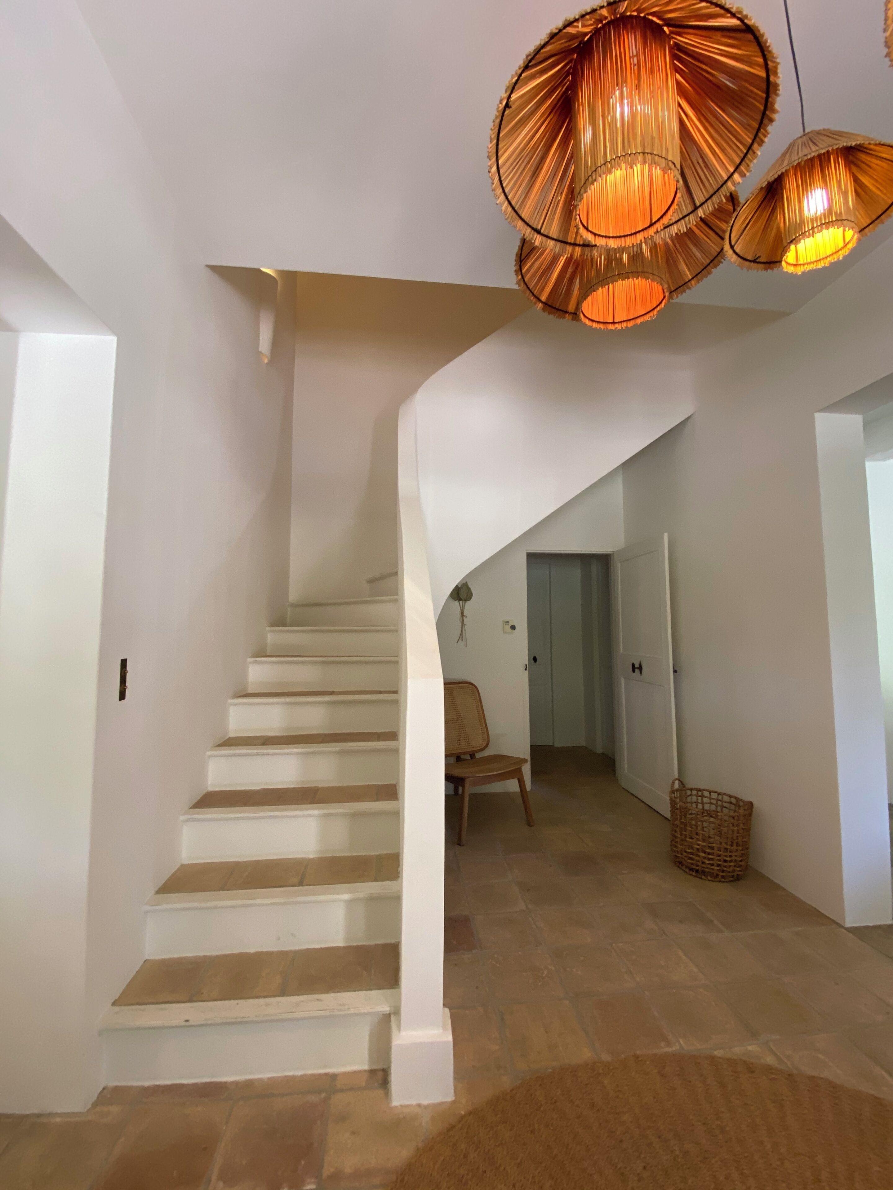 Una escalera con paredes blancas y piso de madera, que conduce a una habitación con una puerta y una cesta de mimbre.