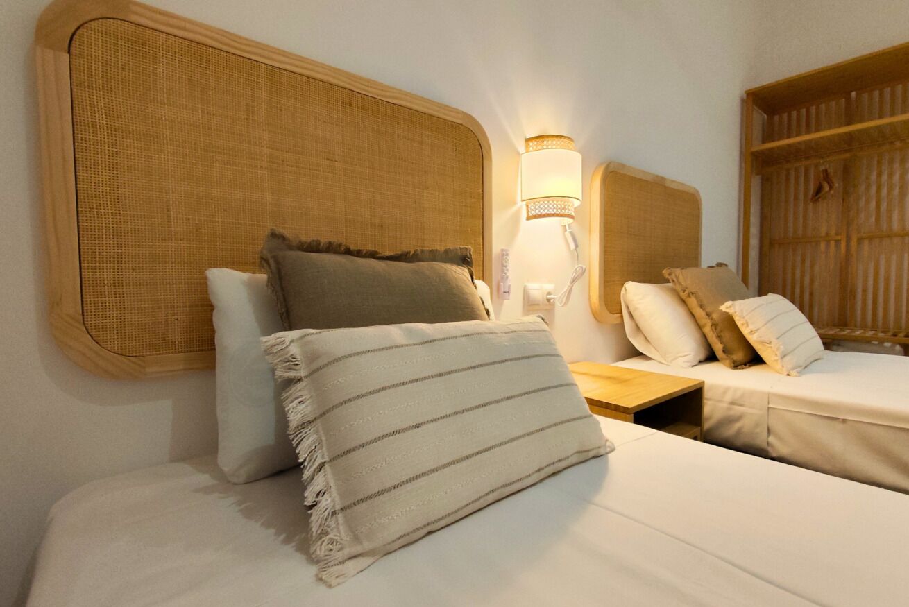 Une chambre d’hôtel avec deux lits, une table de chevet, une lampe et une armoire.