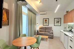 Ein modernes Wohnzimmer mit einer Couch, einem Esstisch mit Stühlen, einer Küchenzeile mit Spüle und Schränken sowie Kunstwerken an den Wänden.