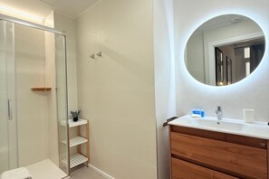 Ein Badezimmer mit Duschkabine aus Glas, einem Holzkosmetikschrank mit Spiegel und einem weißen Waschbecken.