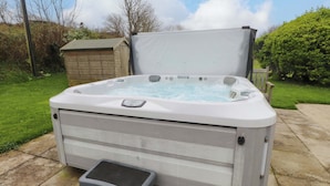 A hot tub with a control panel, a step stool, and a wooden shed in the background. - Belan Wen (Beaumaris)