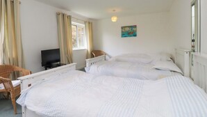 Un dormitorio con dos camas, una televisión, una silla de mimbre y un cuadro en la pared.