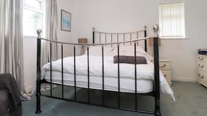 A single bed with a metal frame, a bedside table, a nightstand, a window with blinds, and a hanging light fixture. - Belan Wen (Beaumaris)
